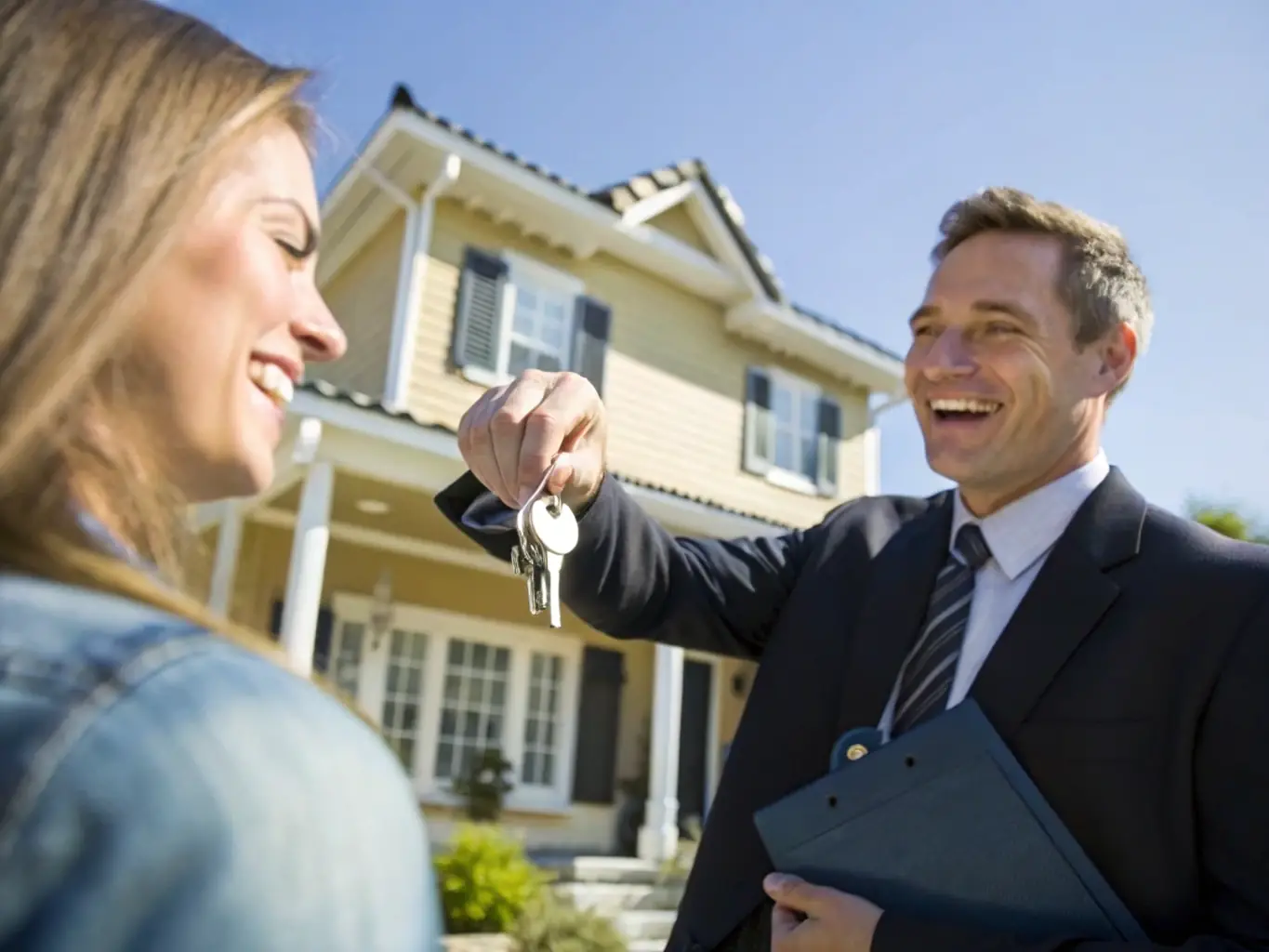 A professional real estate agent handing over keys to a smiling couple in front of their new home, bathed in warm sunlight, symbolizing the joy and security of a successful residential real estate transaction facilitated by Sterling National Title.